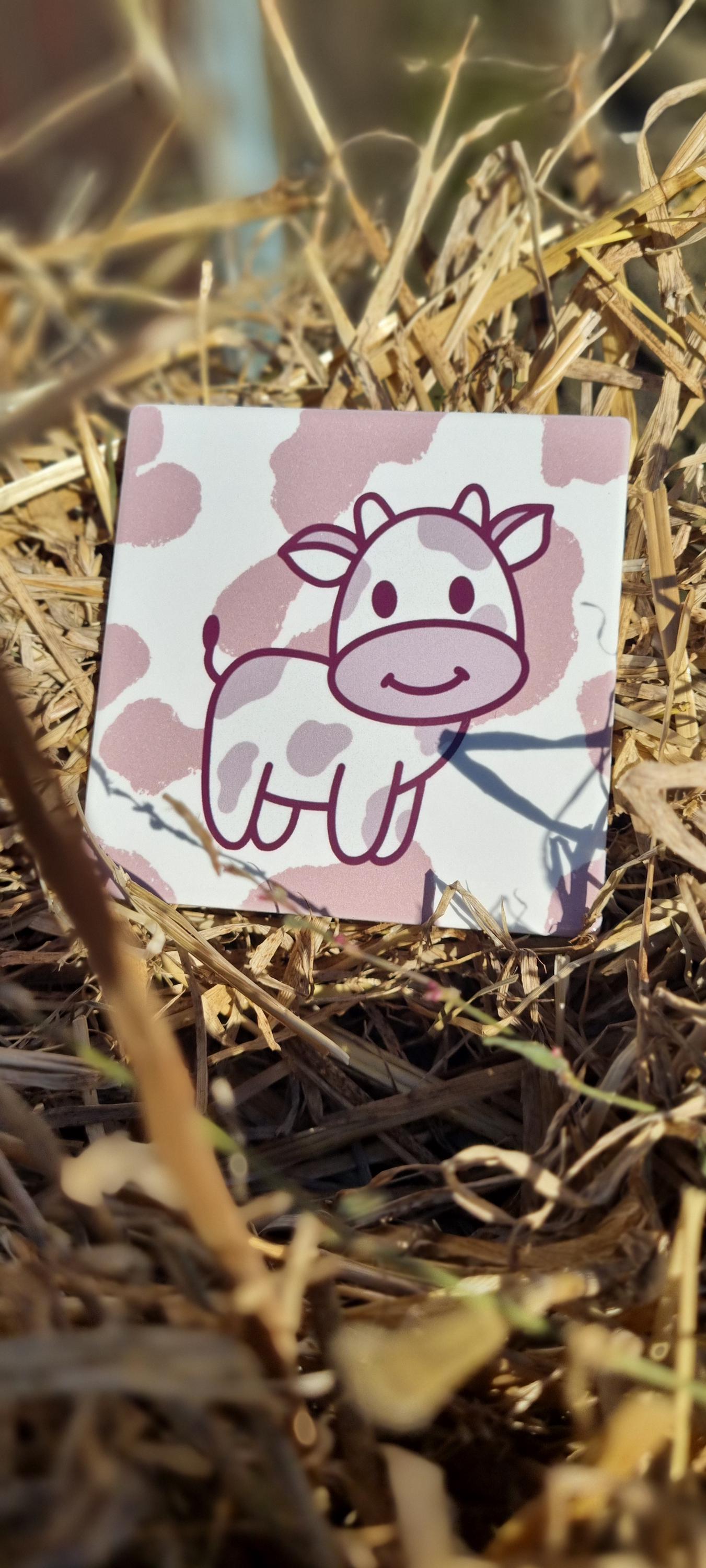 Cute cow design animal lover coaster with pink and white pattern placed on dry grass