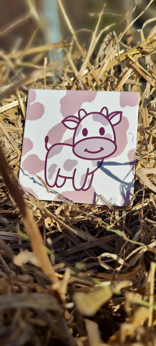Cute cow design animal lover coaster with pink and white pattern placed on dry grass