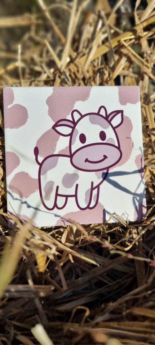 Cute cartoon cow design on an animal lover coaster with pink spots placed on dry grass