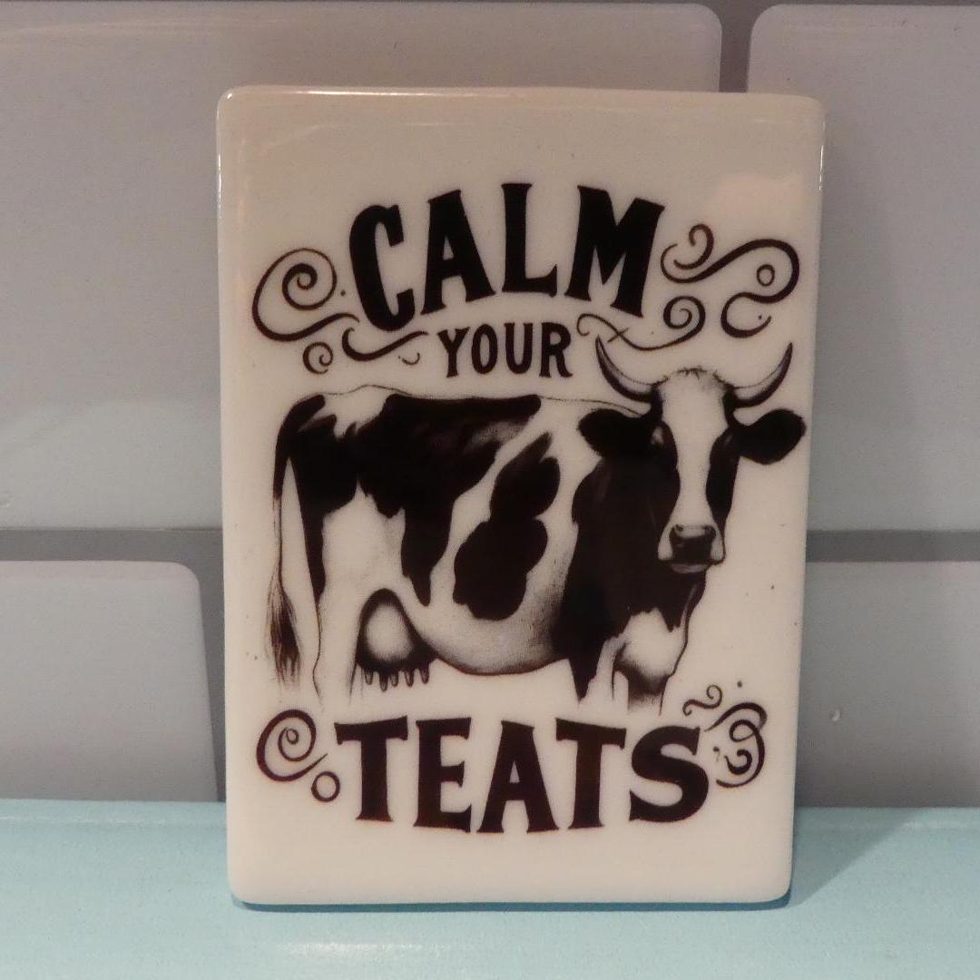 Calm your teats novelty magnet featuring a black and white cow design with decorative text
