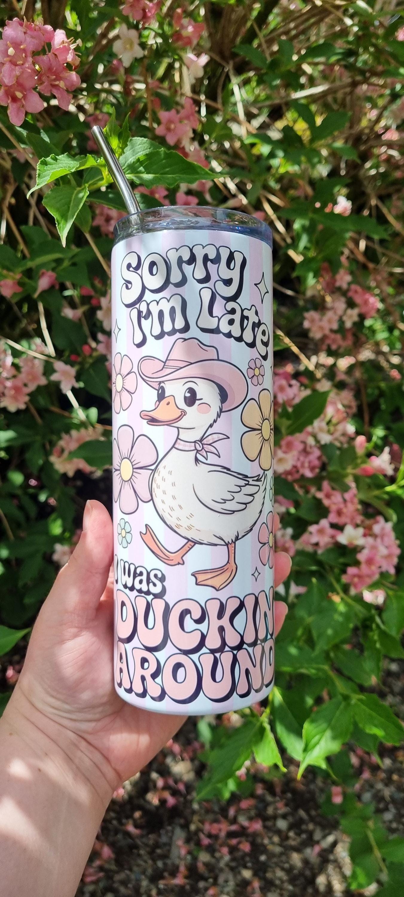 Funny duck tumbler with cartoon duck wearing a pink hat and 'Sorry I'm Late' text held outdoors
