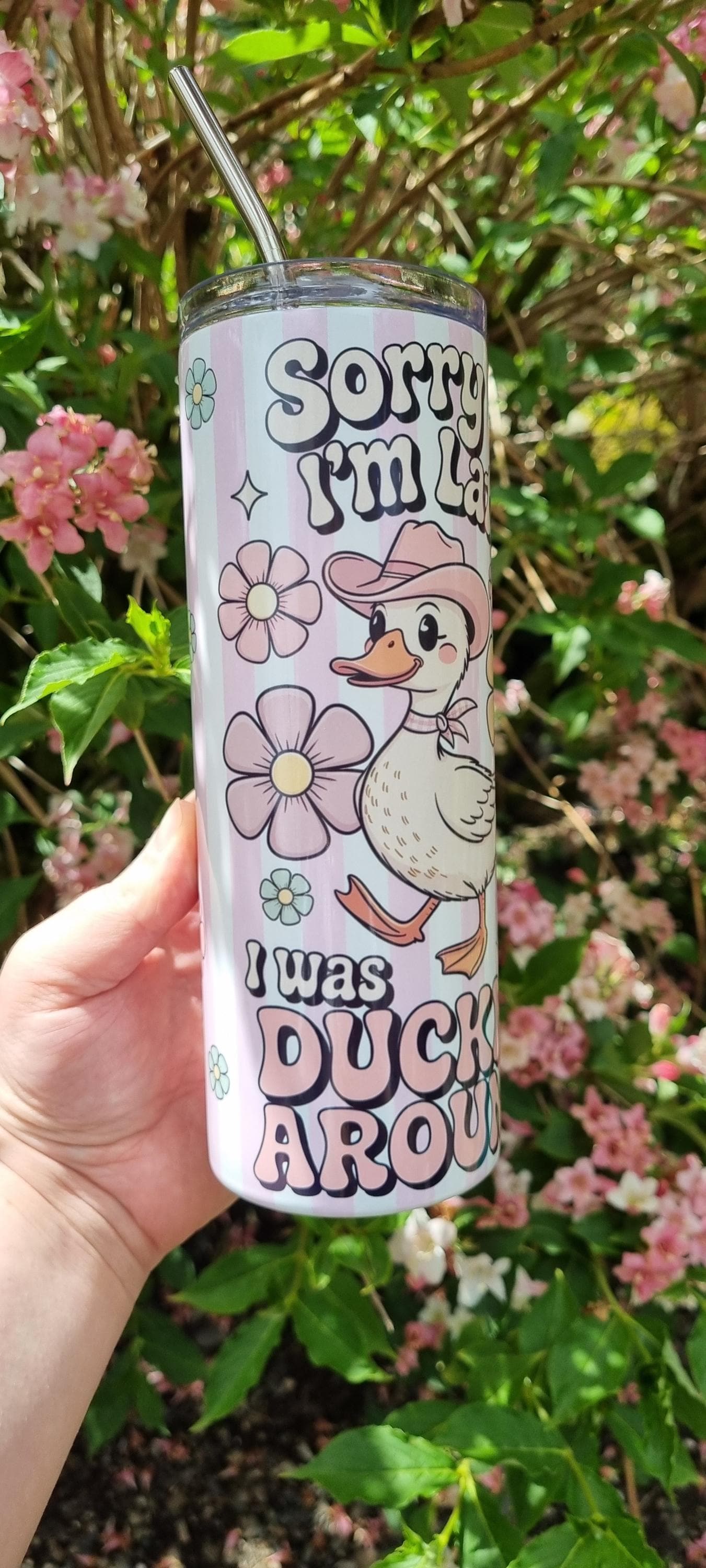 Funny duck tumbler with cartoon duck and floral design held outdoors with pink flowers