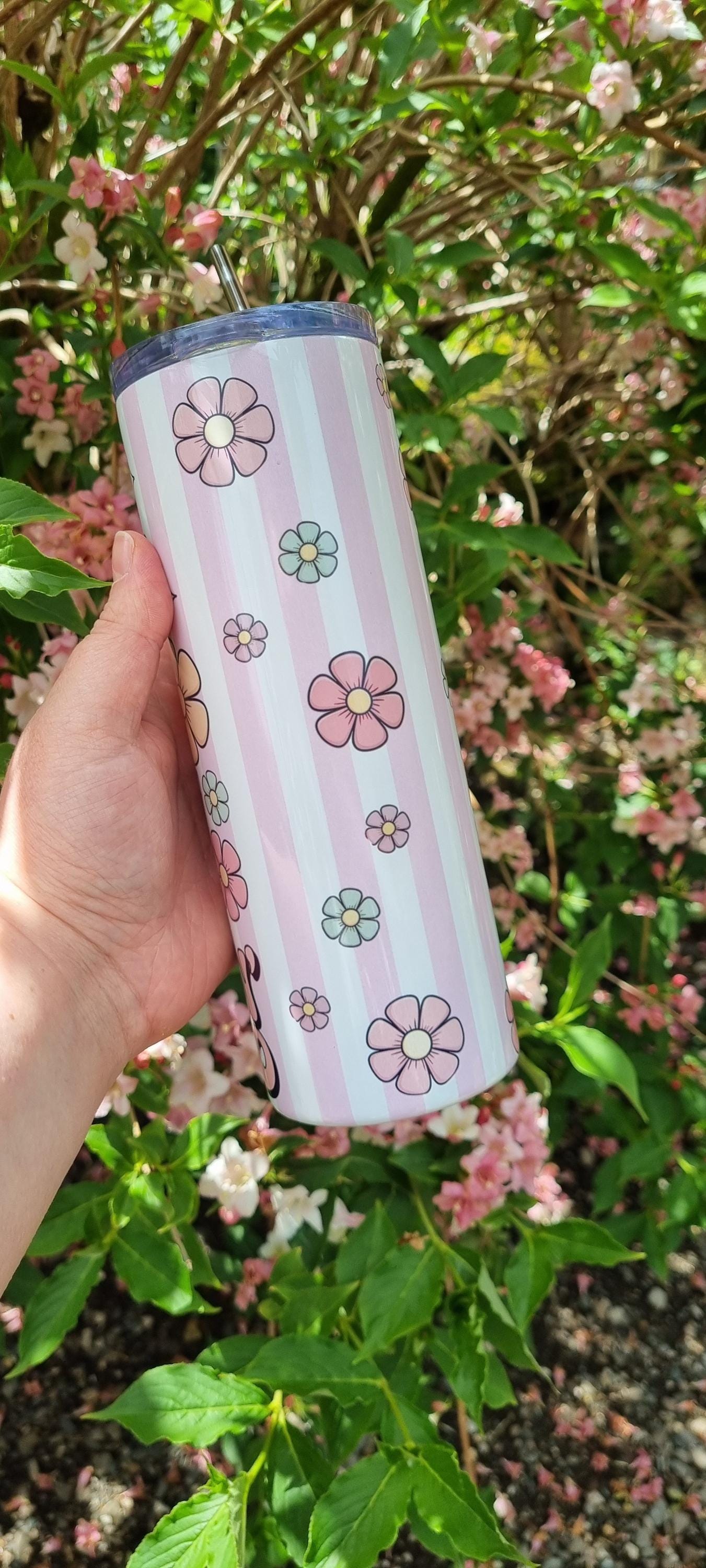 Hand holding a pastel striped funny duck tumbler decorated with pink and blue flowers outdoors