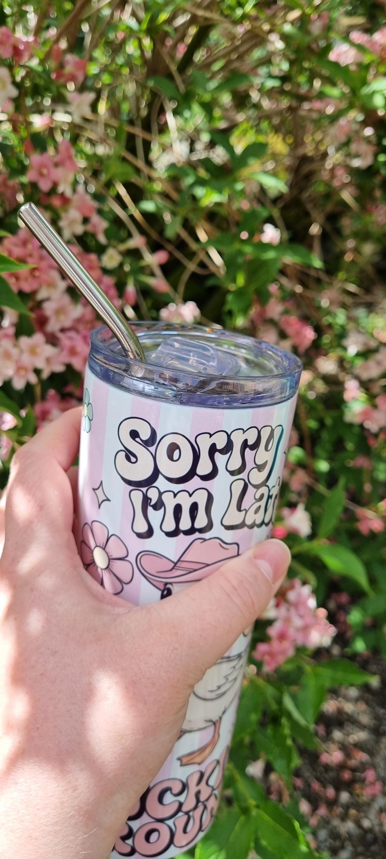 Funny duck tumbler with straw and humorous Sorry I'm Late design held outdoors near pink flowers