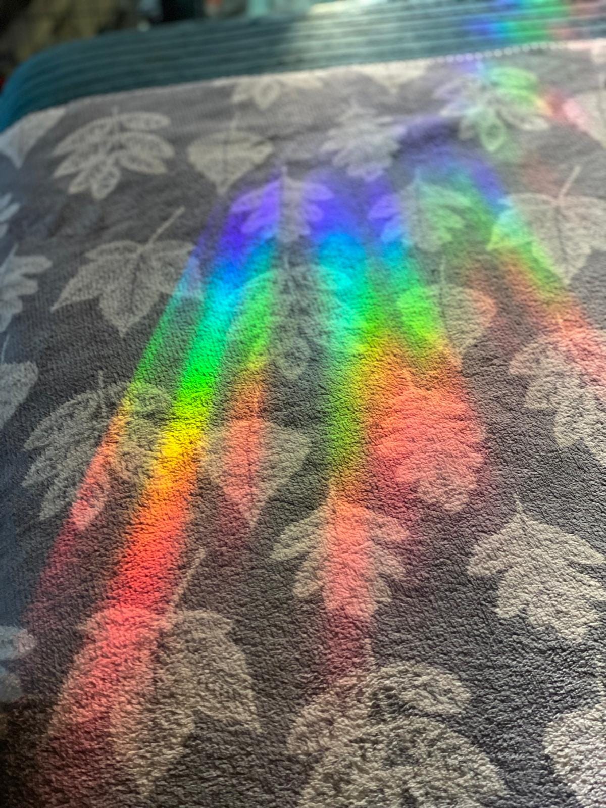Rainbow light reflection created by gold gonk suncatcher on textured floral fabric