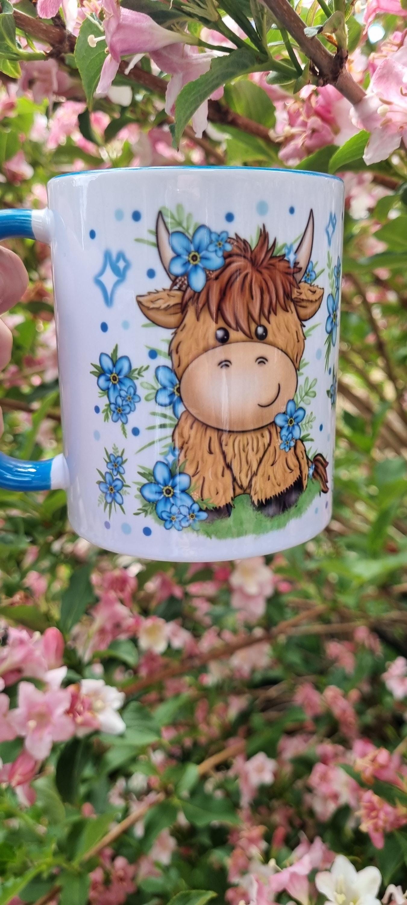Ceramic mug featuring cute highland cow with blue flowers, a perfect highland cow gift for animal lovers