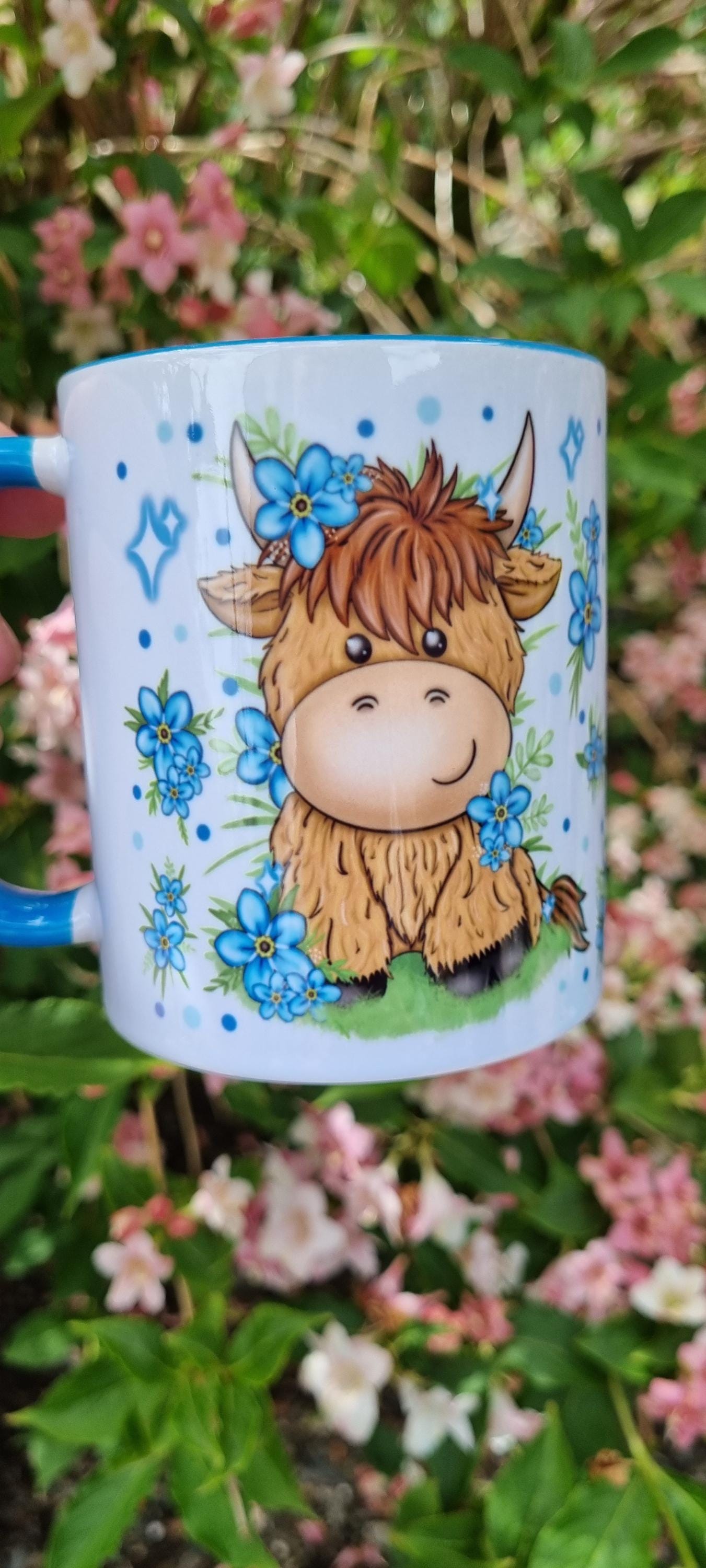 White ceramic mug featuring a cute cartoon highland cow with blue flowers highland cow gift for animal lovers