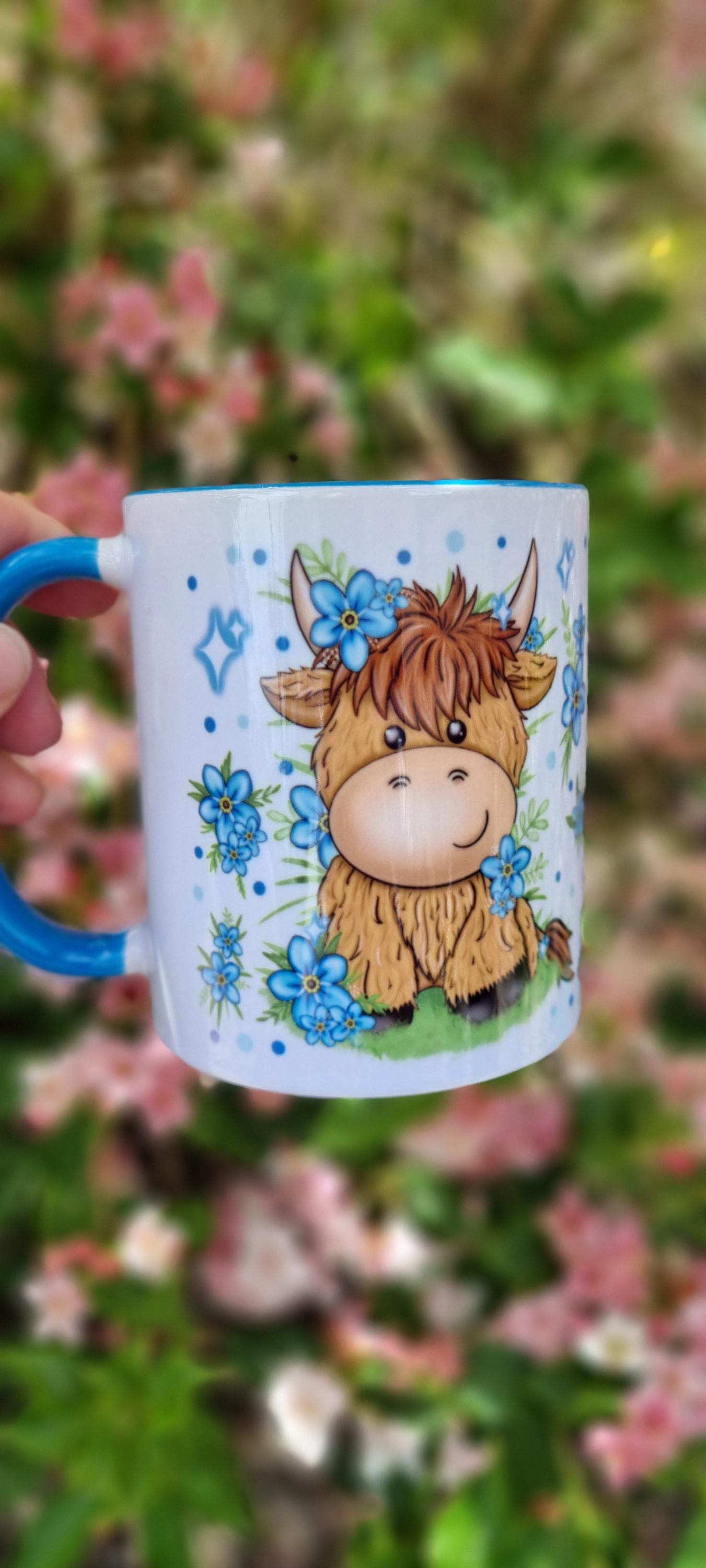 Cute white mug with blue handle featuring a cartoon highland cow with flowers highland cow gift for animal lovers