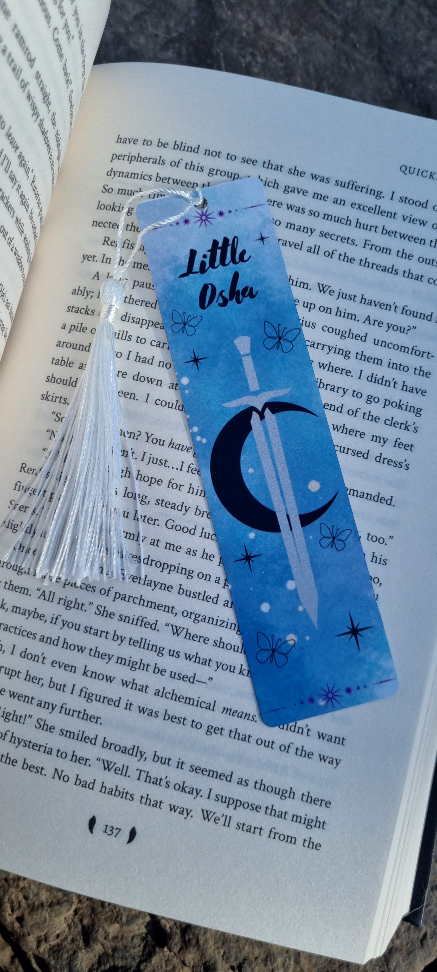Little Osha book gift blue bookmark with sword and moon design and white tassel on open book page