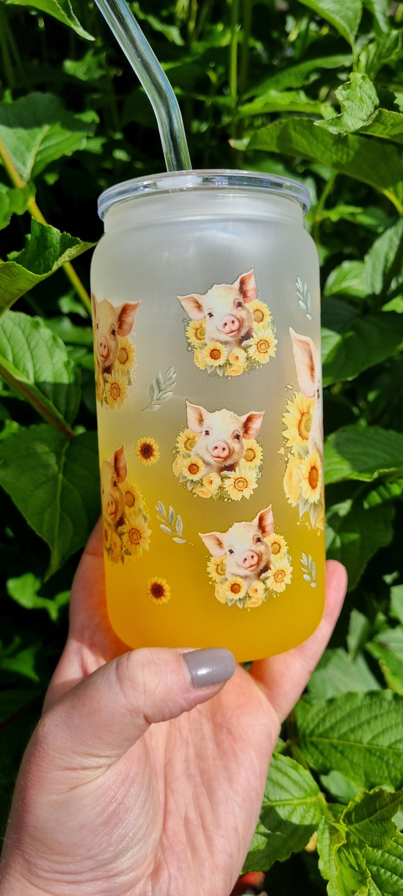 Pig sunflower glass tumbler with frosted design and yellow gradient held outdoors with straw