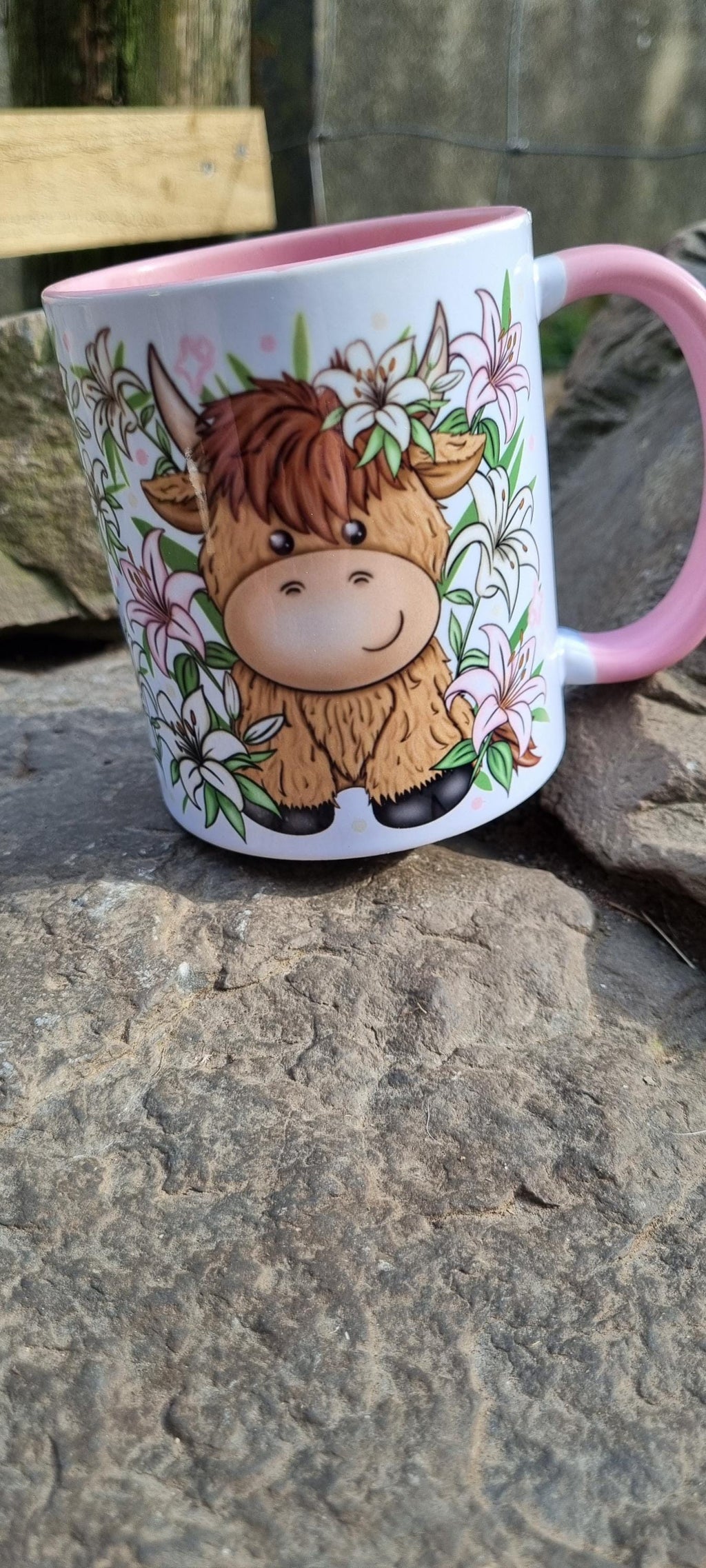 Pink highland cow mug with cartoon cow design and floral accents on stone surface