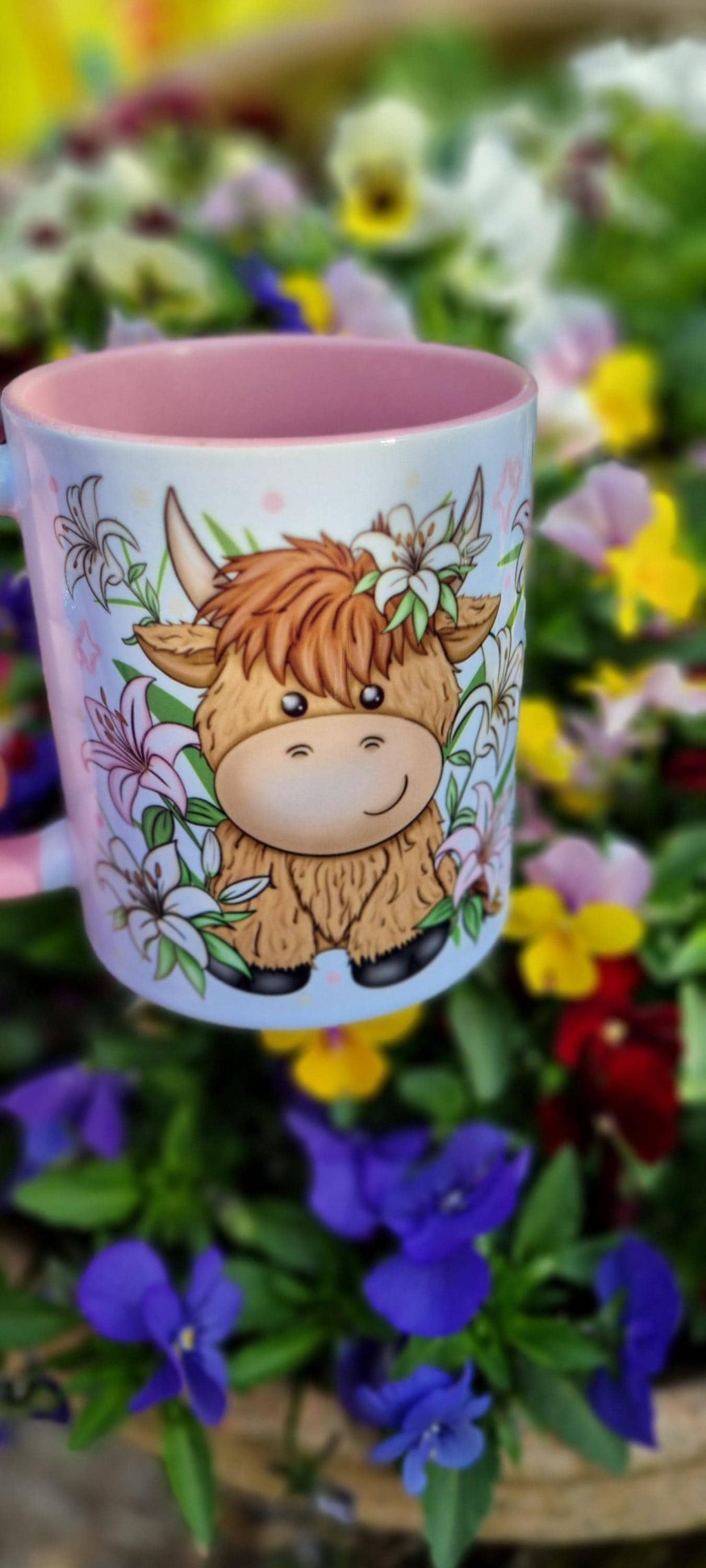 Pink highland cow mug with cute cartoon cow and floral design on a blurred flower background