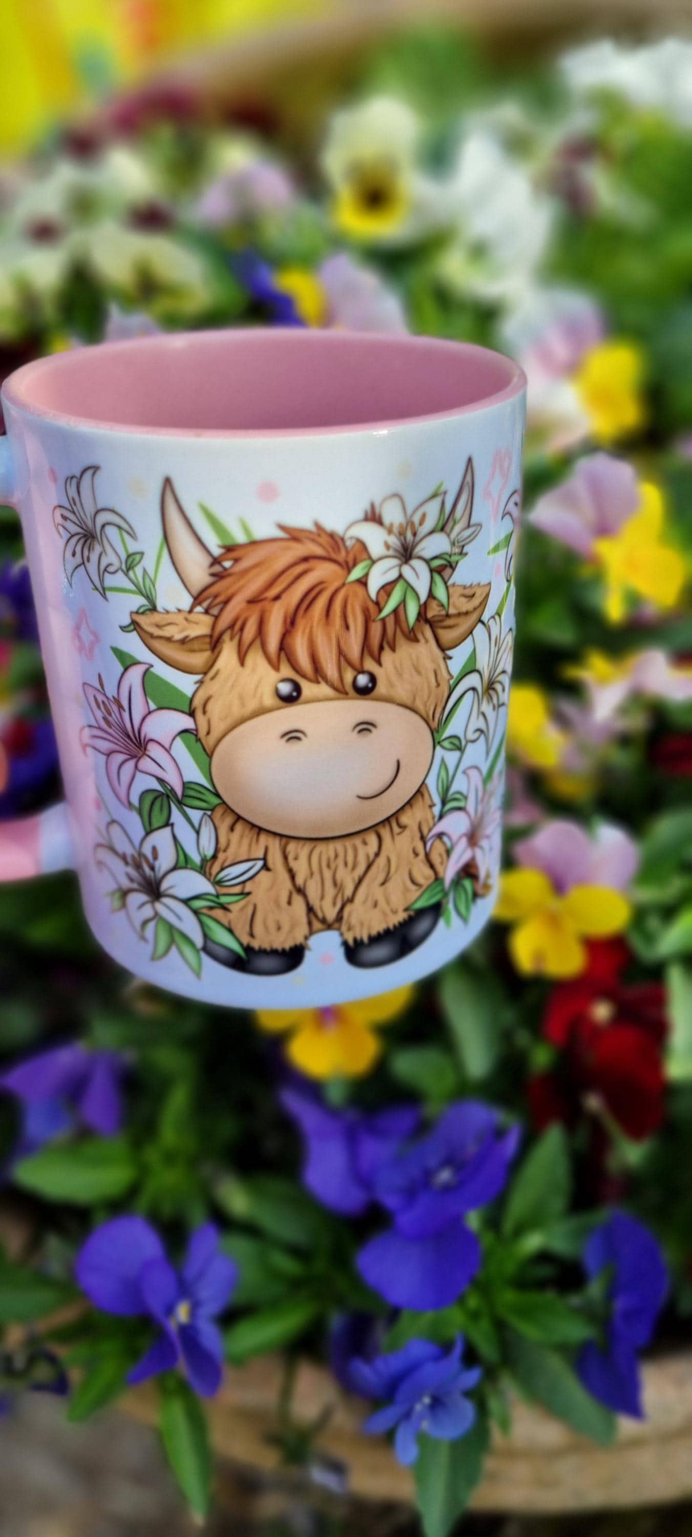 Pink highland cow mug with cute cartoon cow and floral design on a blurred flower background