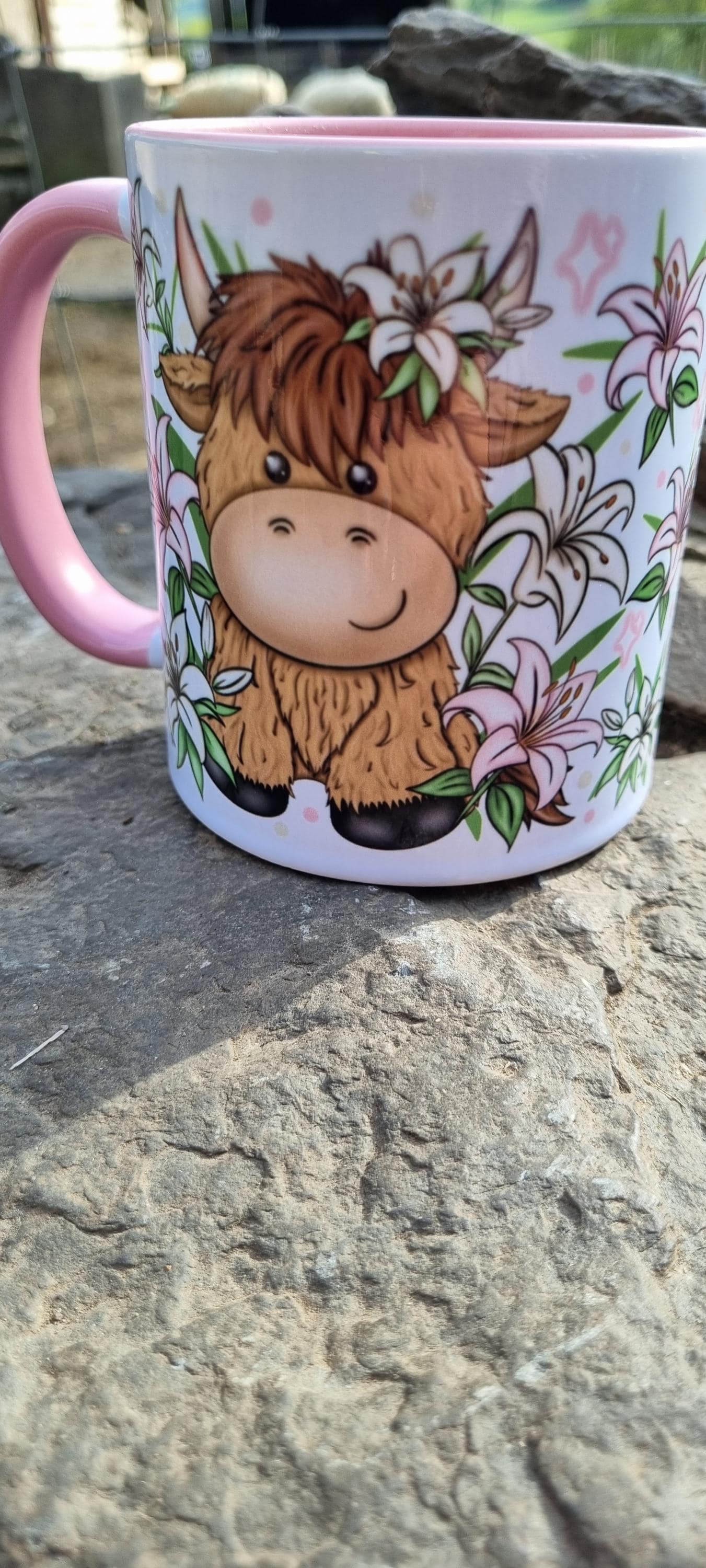Pink highland cow mug with cute cartoon cow and floral design on outdoor stone surface