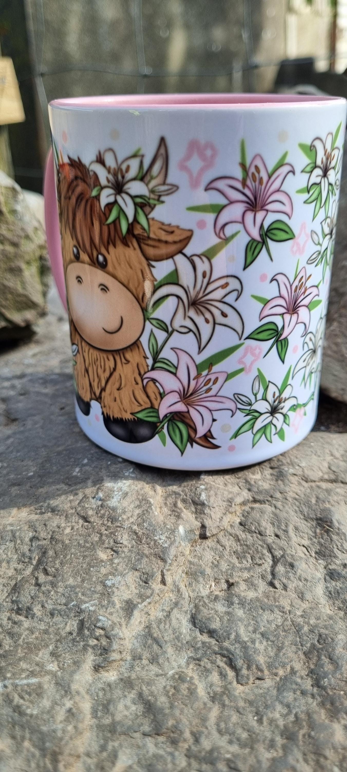 Pink highland cow mug with cute cartoon cow and pink lilies design on white background