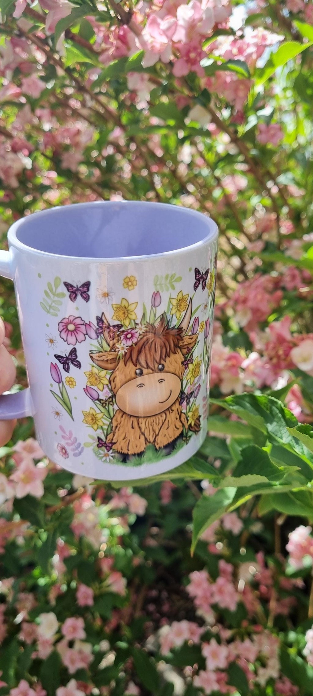 Spring cow coffee cup with cute cow and floral design held outdoors among pink blossoms