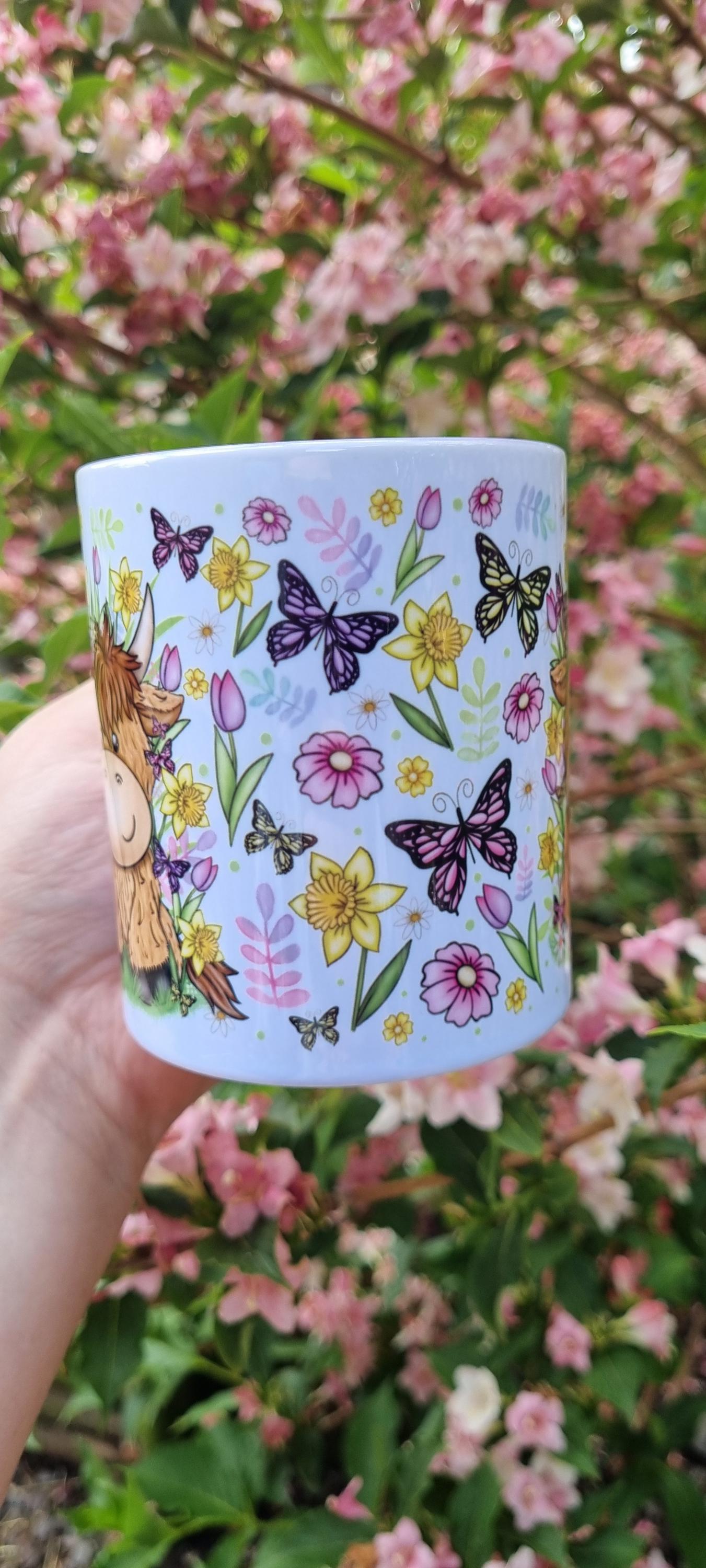 Spring cow coffee cup with colourful butterflies and floral design held outdoors with pink blossoms