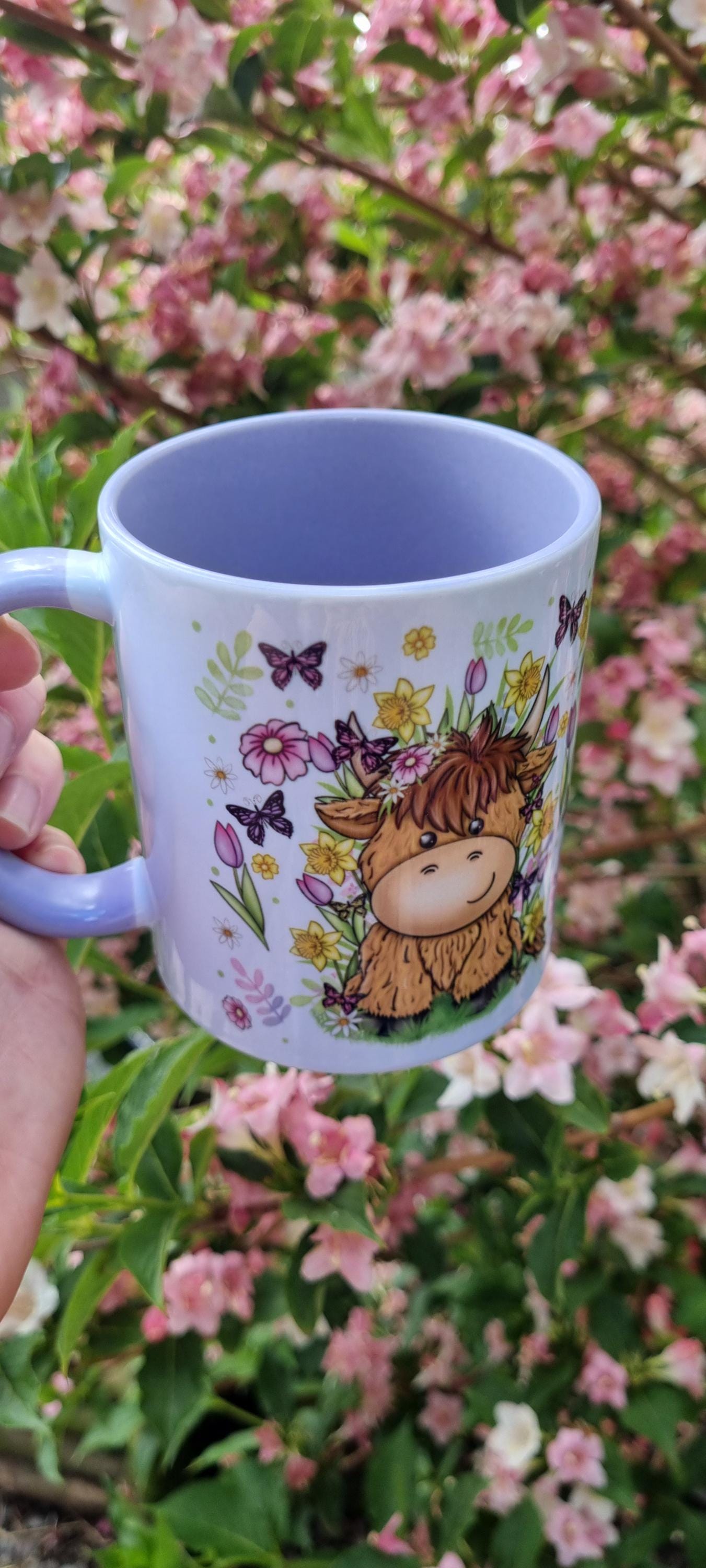 Spring cow coffee cup with cute cow and floral design held outdoors with pink flowers background