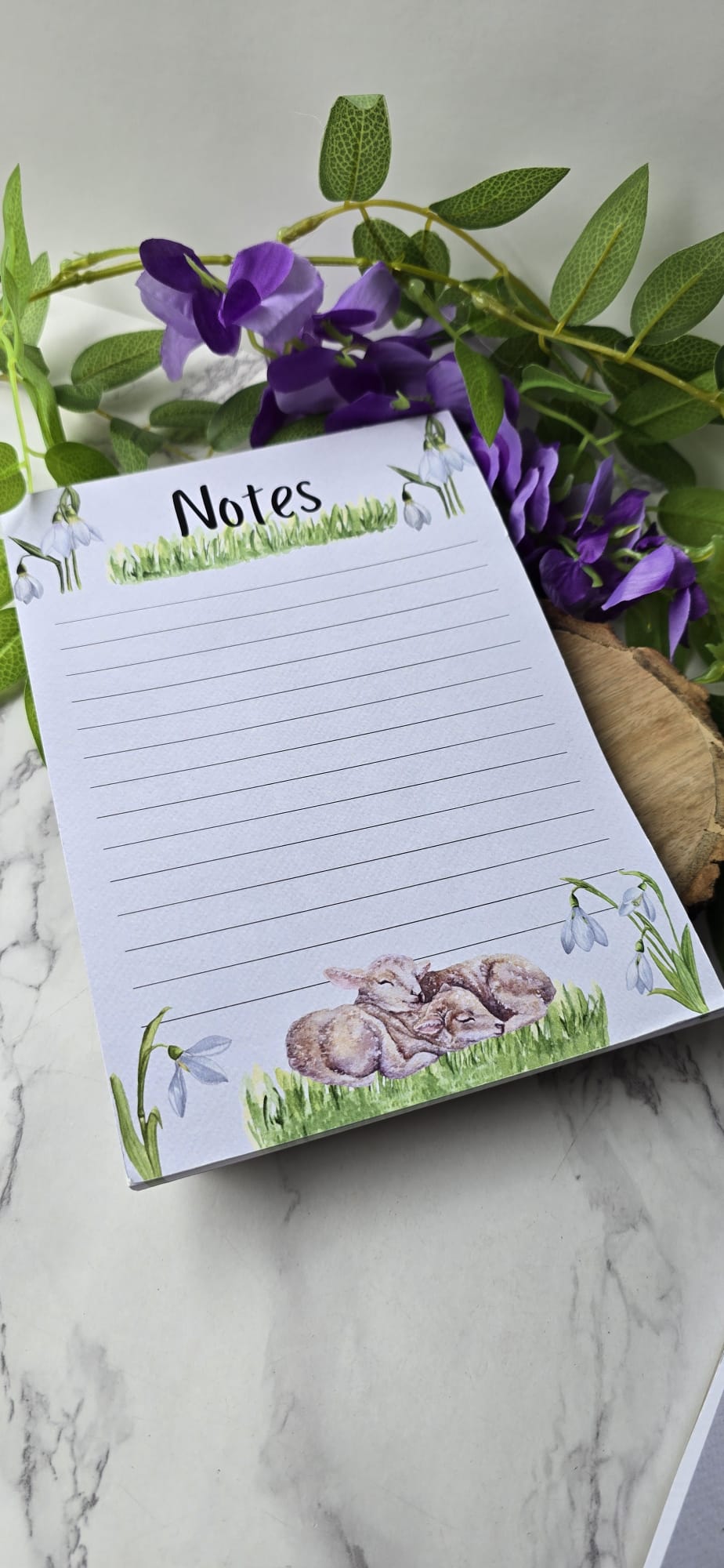Spring lamb notepad with floral design and lined pages surrounded by purple flowers and green leaves