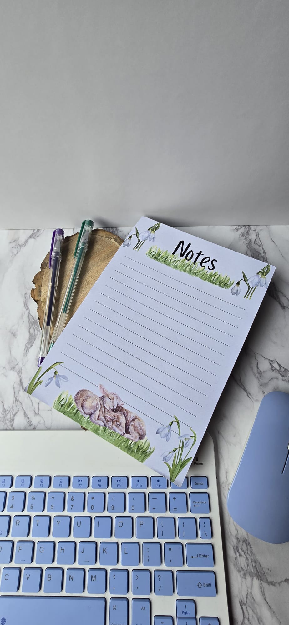 spring lamb notepad with floral and lamb design beside pens and keyboard on marble surface