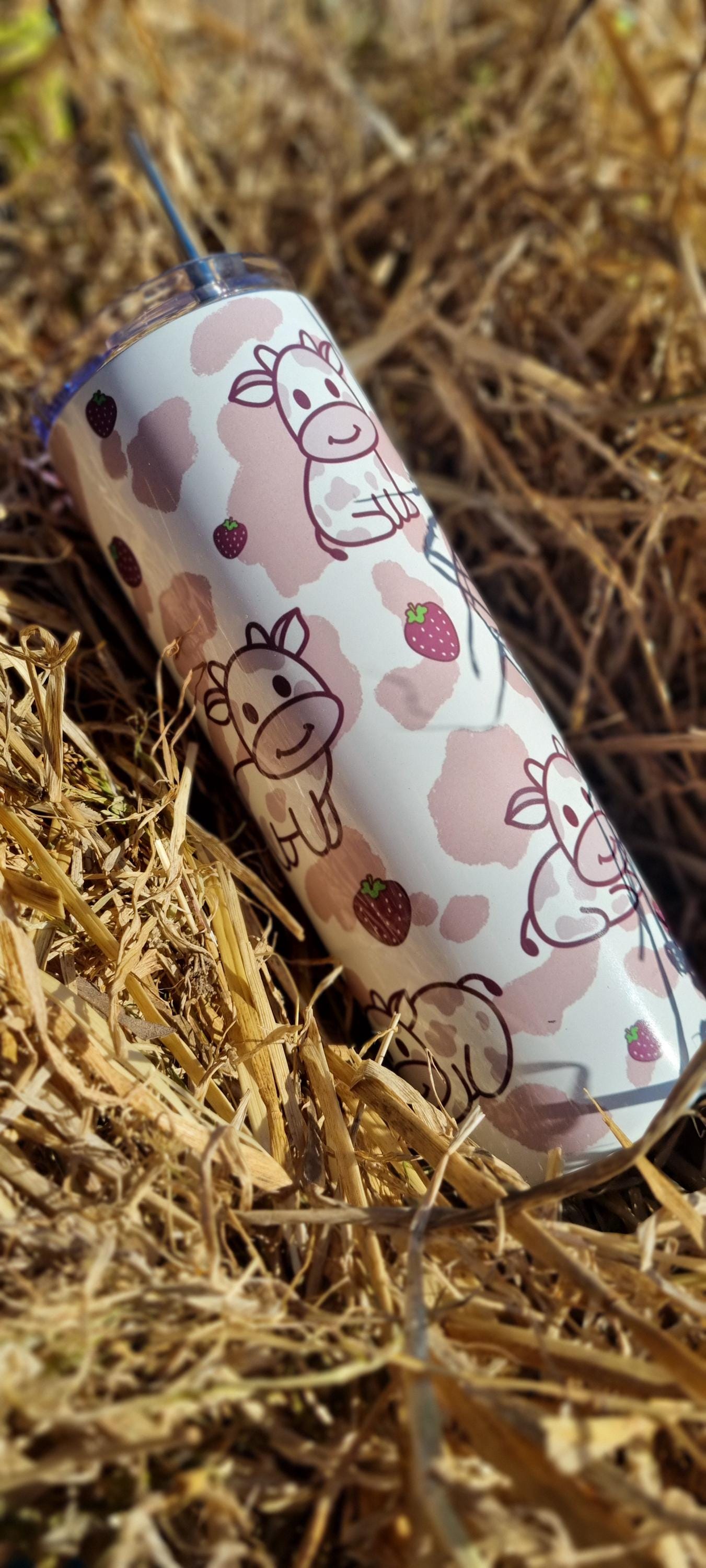 Strawberry cow tumbler with cute cow and strawberry design placed on dry grass