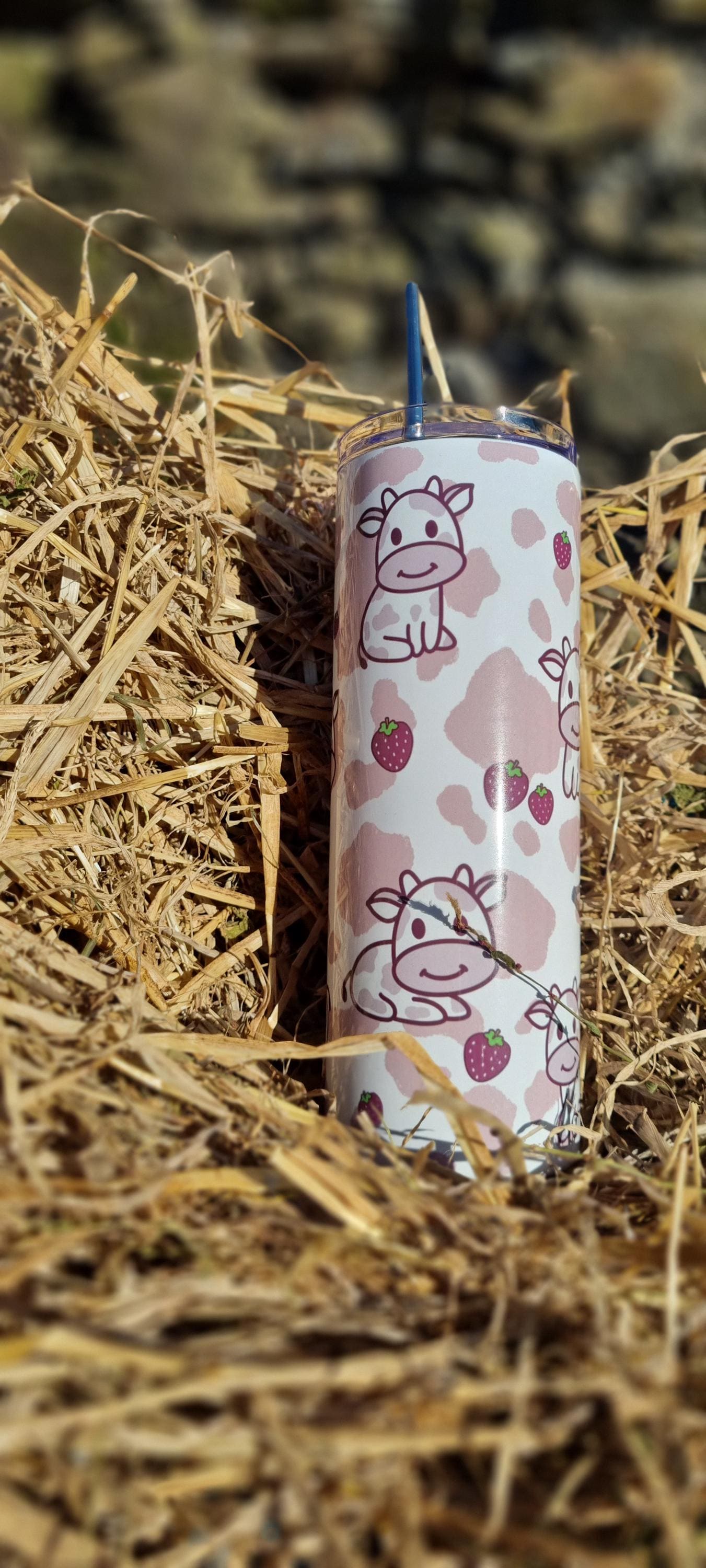 Strawberry cow tumbler with pink cow and strawberry design placed on dry hay outdoors