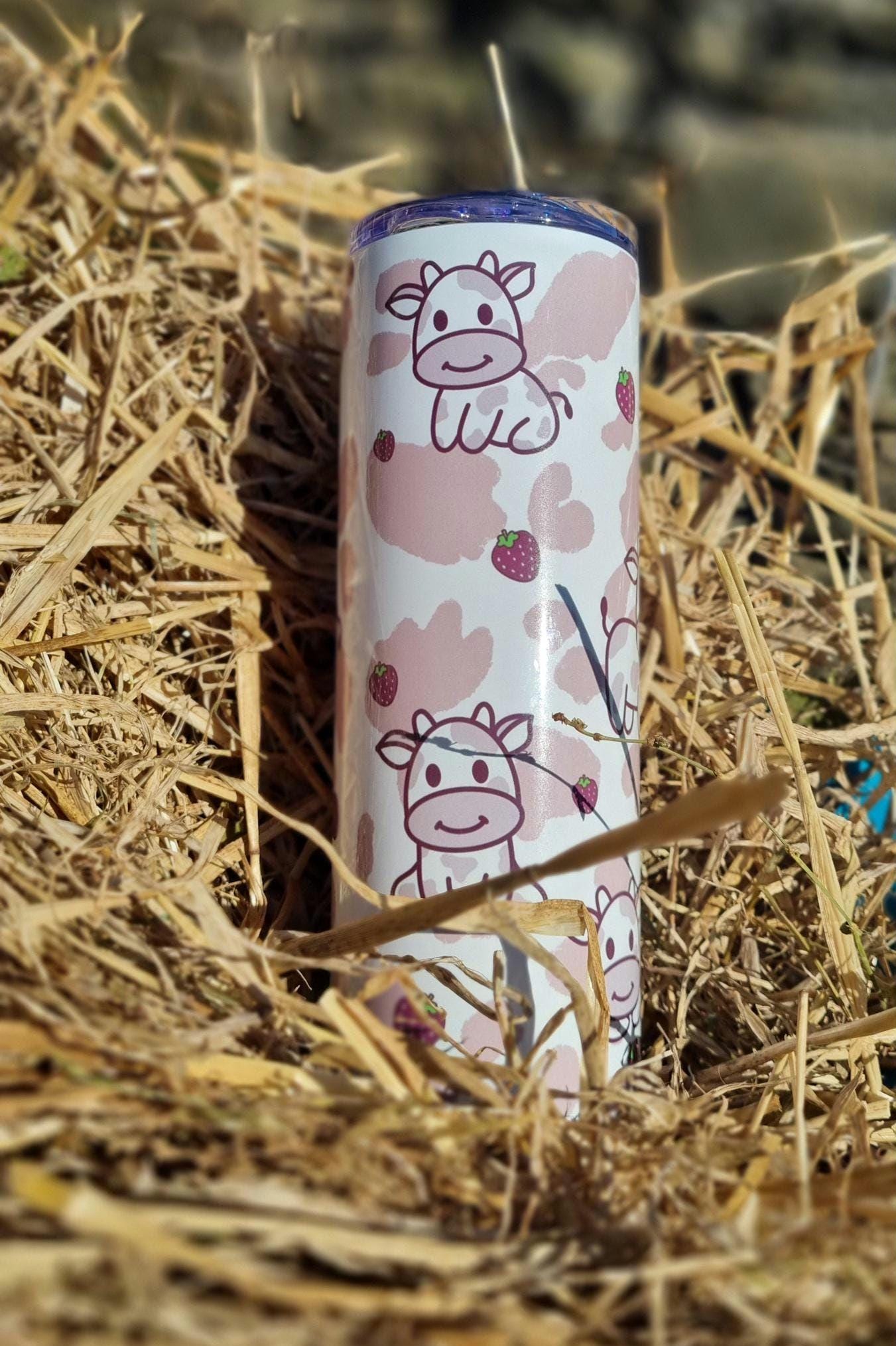 Strawberry cow tumbler with cute cow illustrations and strawberry patterns on a natural straw background