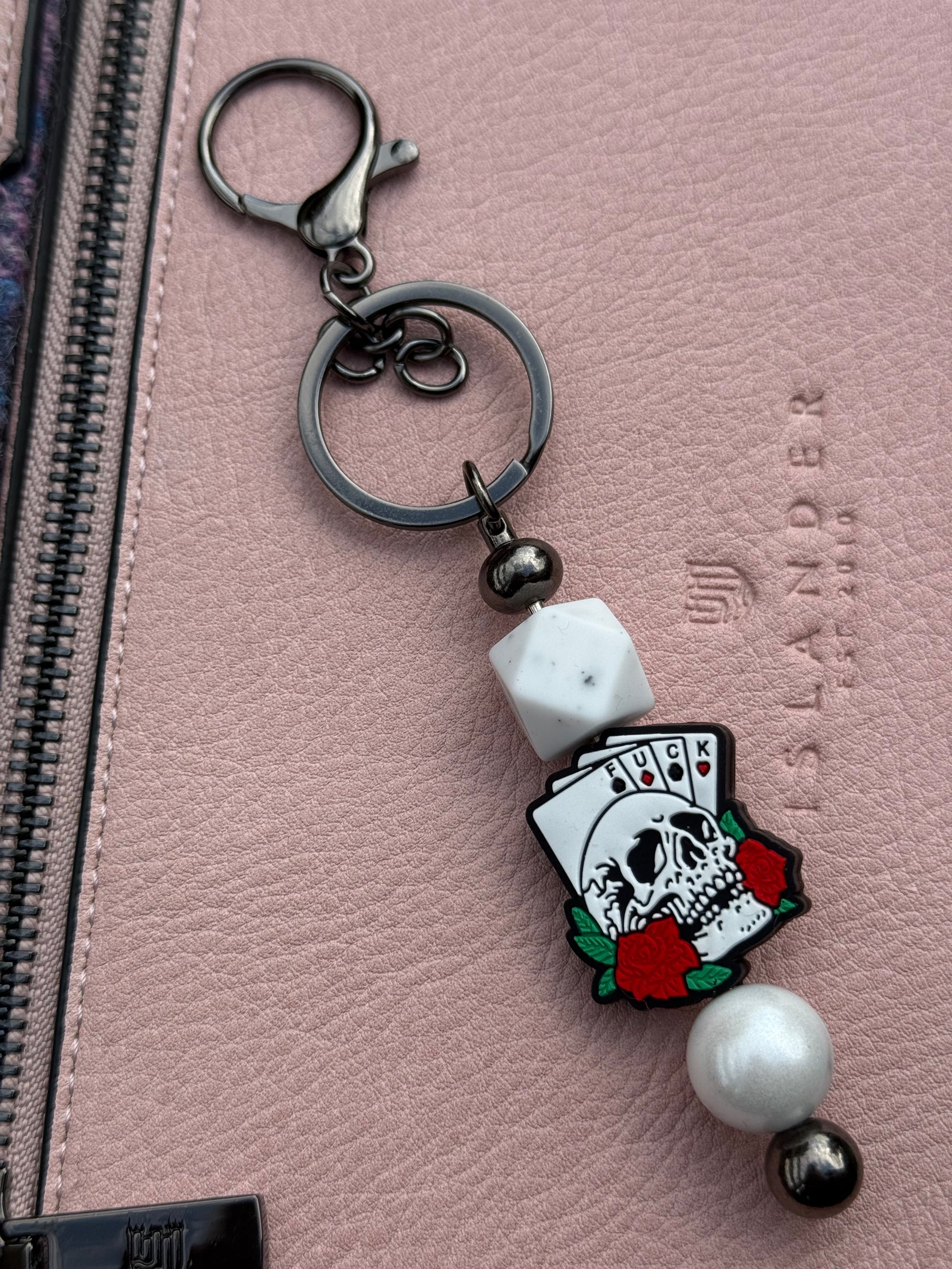 Morally grey fantasy book accessory keychain with skull card design and beads on pink textured surface
