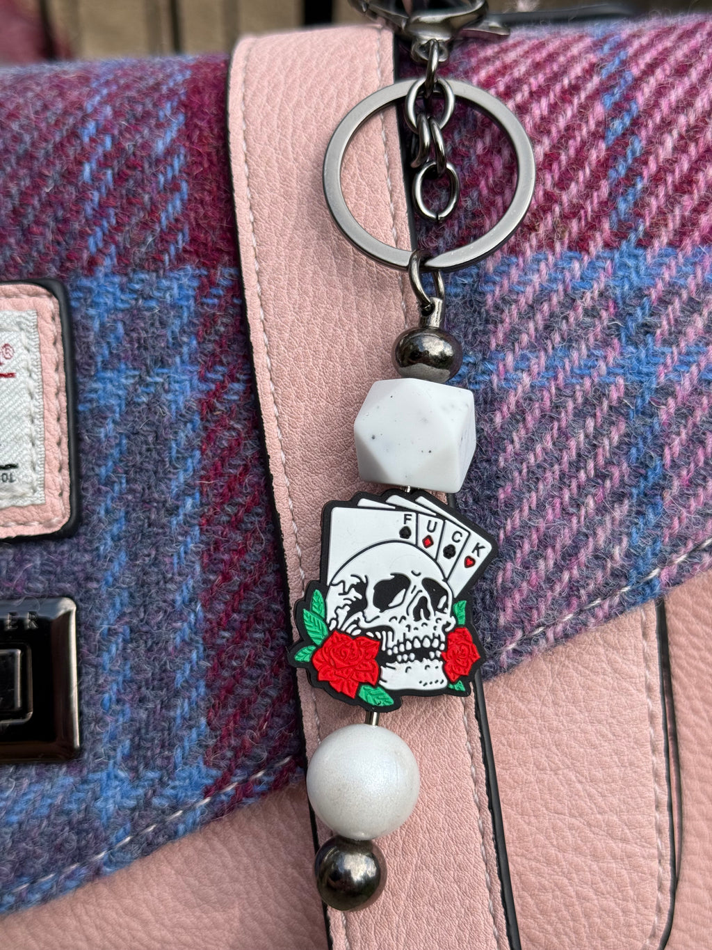Morally grey fantasy book accessory keychain with skull, playing cards, and red roses on a pink and purple plaid bag