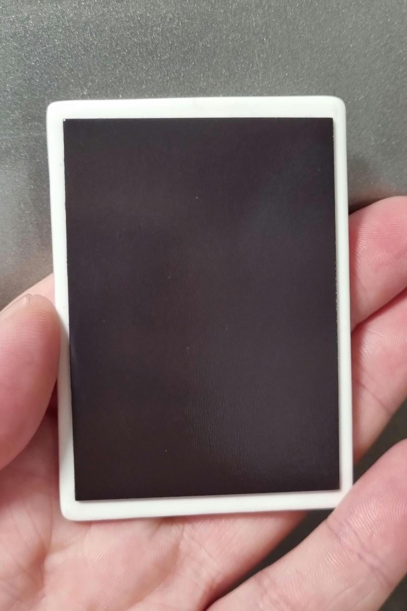Hand holding a rectangular witchy tarot fridge magnet with a plain black surface and white border
